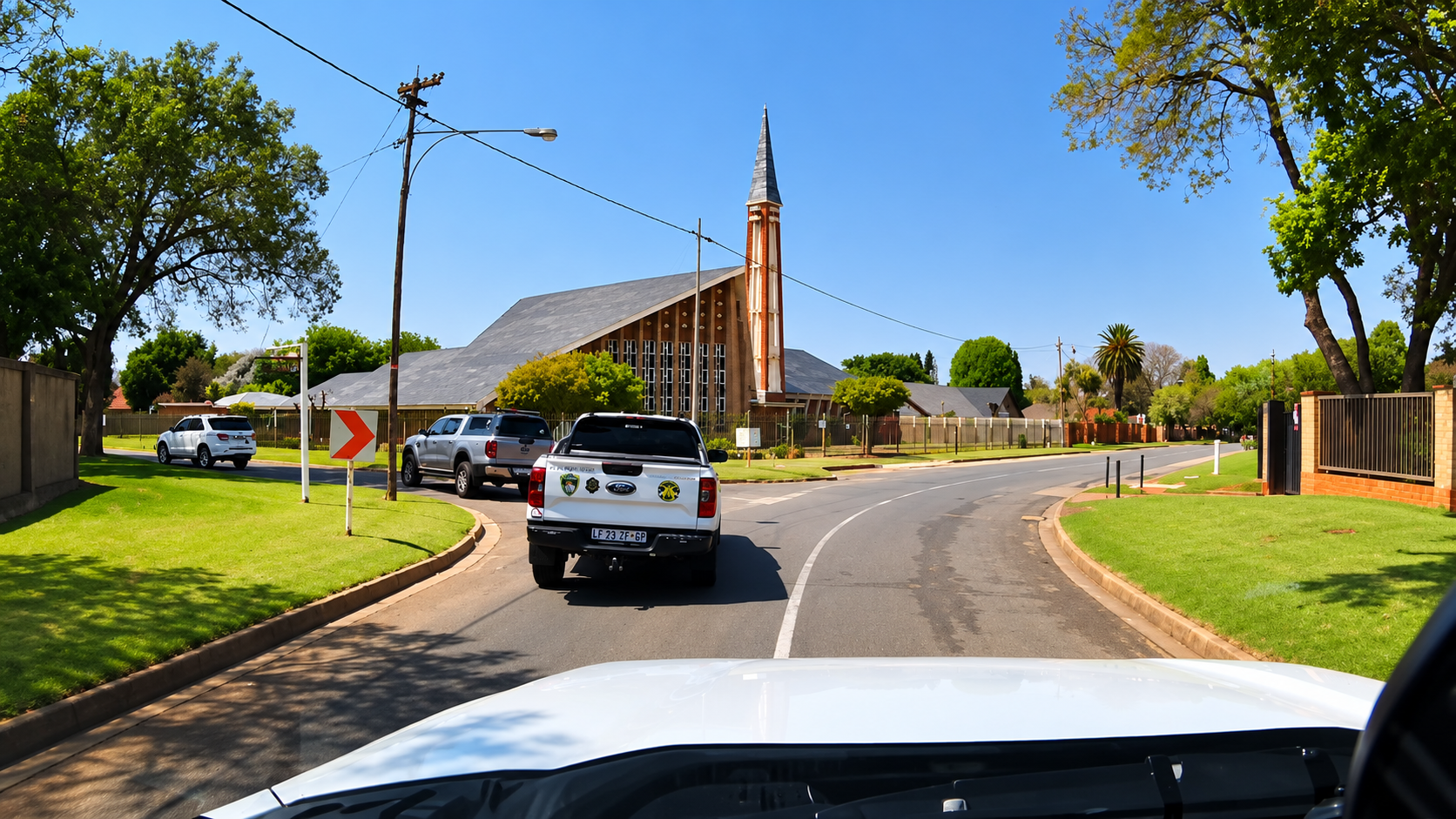 View from a following vehicle behind a response bakkie on a suburban road beside a church