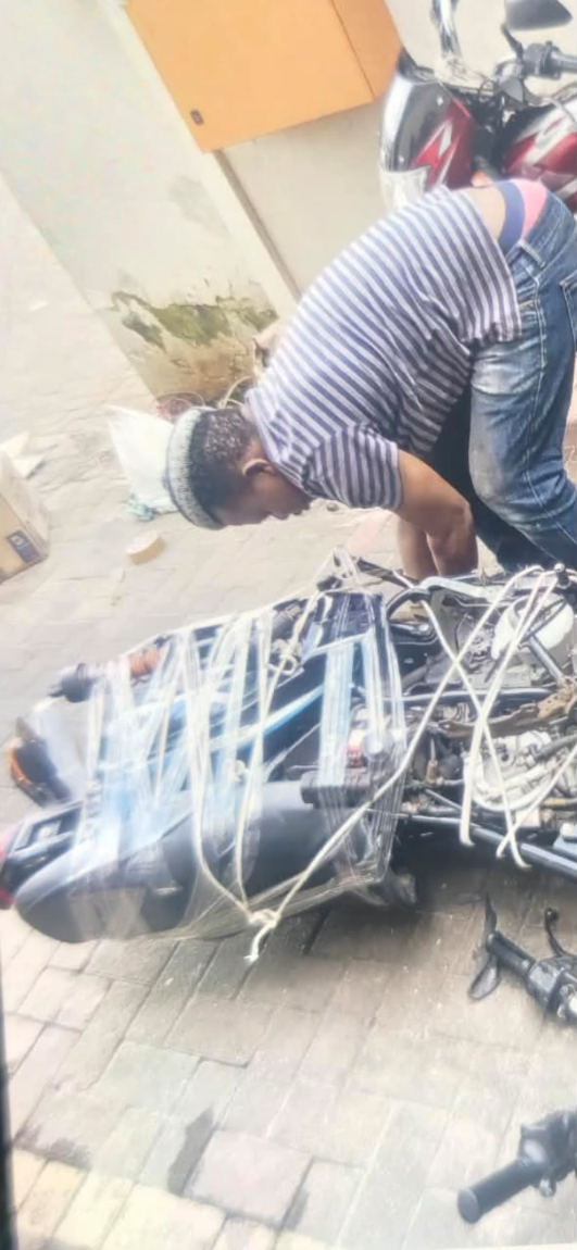 A man bent over a stripped motorcycle wrapped in plastic and rope