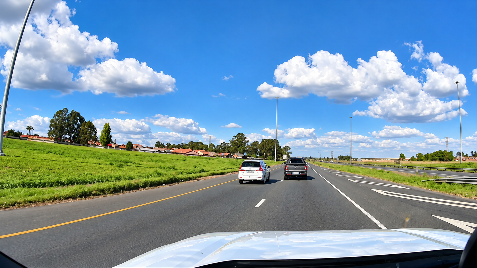 View from a pursuing vehicle on a highway behind a white car and a grey bakkie